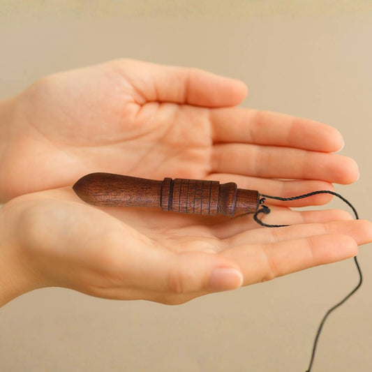 Pêndulo de madeira Mestre pousado nas mãos abertas, simbolizando conexão energética, presença e consciência na prática de Radiestesia Consciente – método TILGUTI.